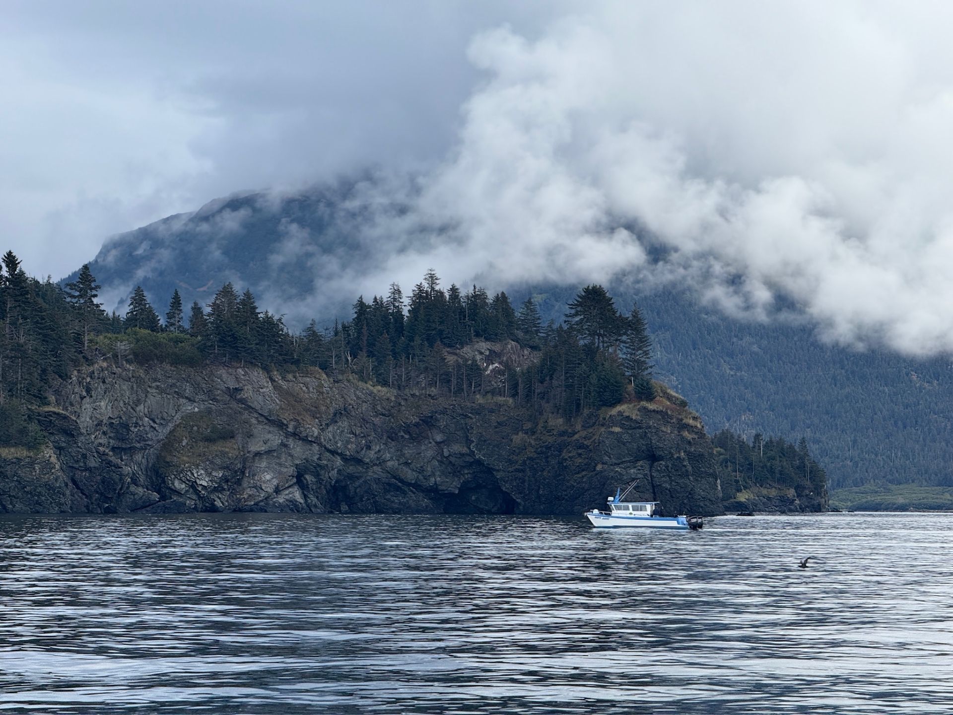 Fishing boat near rocky Alaska coastline with misty mountains