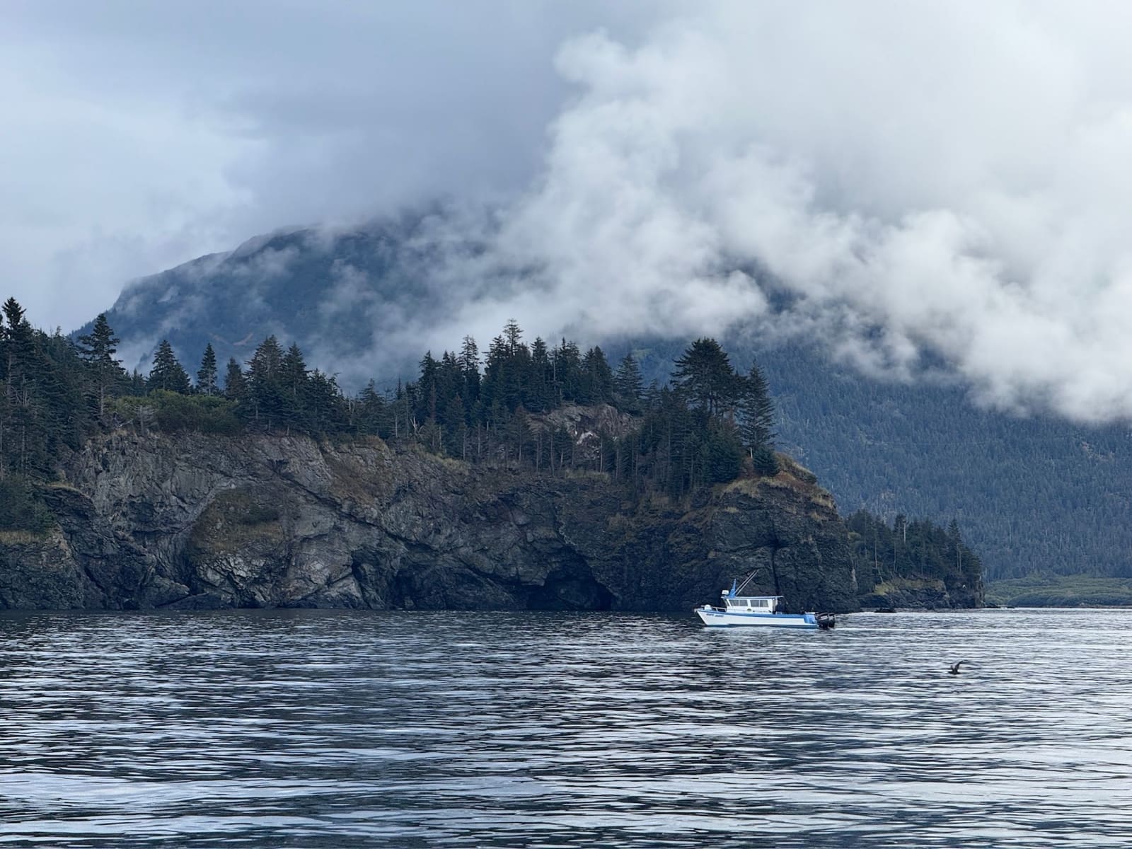 Fishing boat near rocky Alaska coastline with misty mountains
